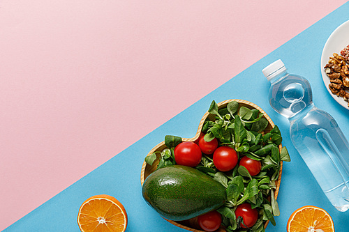 flat lay with vegetable salad, oranges, water and nuts on pink and blue background