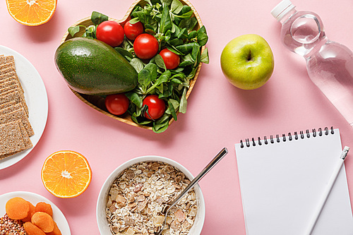 top view of fresh diet food, blank notebook with pencil and water on pink background