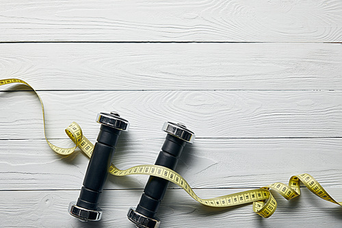 top view of measuring tape and dumbbells on wooden white background with copy space