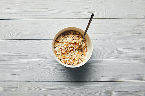 top view of breakfast cereal in bowl with spoon on wooden white background