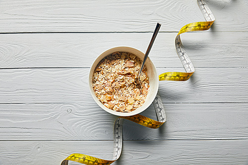 top view of measuring tape, spoon and breakfast cereal in bowl on wooden white background