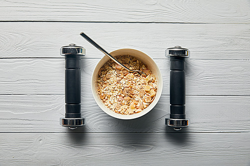 flat lay with breakfast cereal in bowl and dumbbells on wooden white background