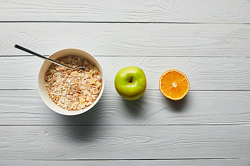 flat lay with breakfast cereal in bowl, apple, orange on wooden white background