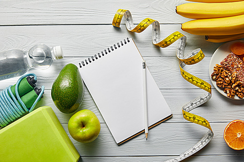 top view of diet food near measuring tape, notebook and sport equipment on wooden white background