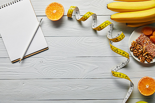 top view of measuring tape, diet food and blank notebook on wooden white background with copy space