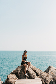 female tourist sitting on rocks and looking at the ocean