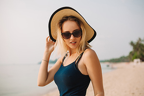 portrait of attractive woman in hat and sunglasses on sandy ocean beach
