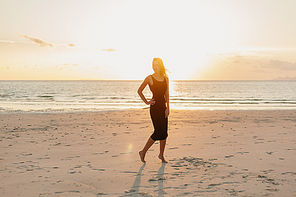 attractive woman standing on ocean beach in sunbeams during sunset