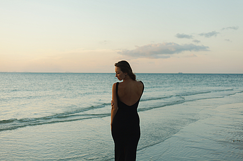 attractive woman standing in dress on ocean beach during sunset