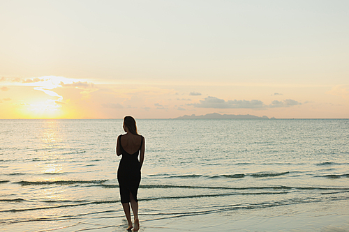 rear view of woman standing in ocean during sunset