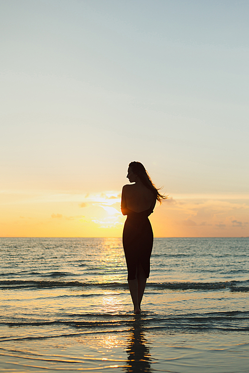 silhouette of girl standing in sea water during sunset