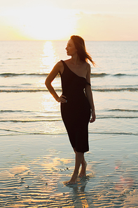 attractive woman posing on ocean beach and looking away during sunset