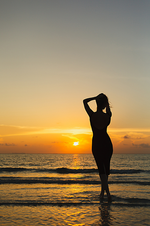 rear view of silhouette of woman posing in ocean during sunset