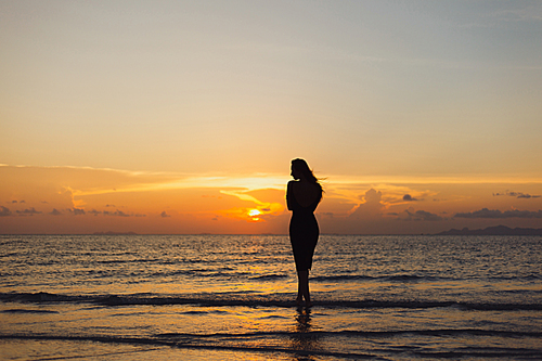 silhouette of woman standing in ocean during beautiful sunset