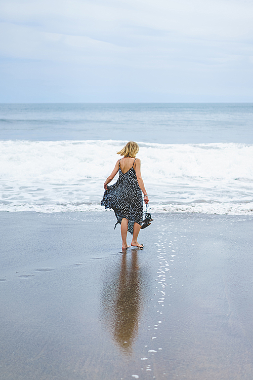 back view of blonde girl in long dress walking near ocean