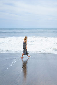 back view of blonde girl in long dress walking near sea