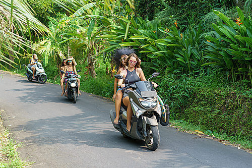 beautiful young women riding motorbikes on road in tropical forest