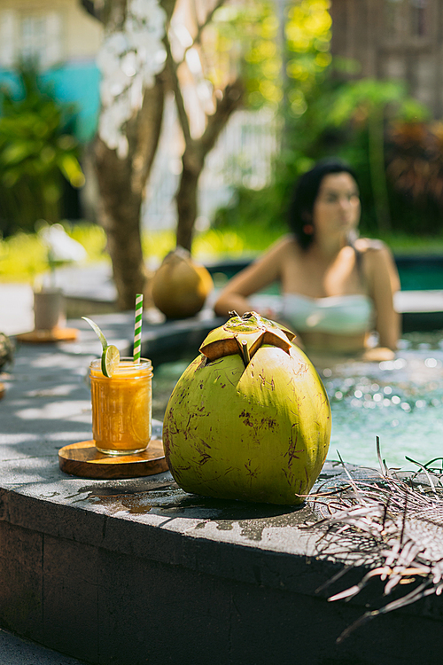 close-up view of fresh tropical cocktails on foreground and woman resting in pool behind