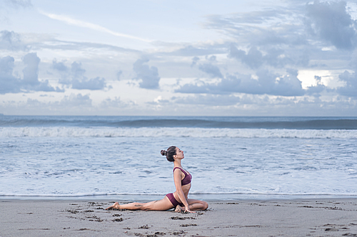 side view of beautiful young woman practicing yoga in sss pose on seashore