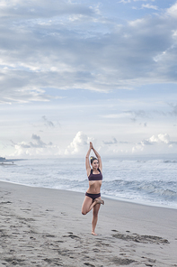 attractive young woman practicing yoga in tree pose (Vrksasana) on seashore