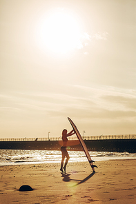 female surfer posing with surfboard on beach at sunset