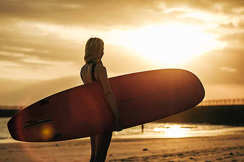 silhouette of surfer posing with surfboard on beach at sunset with back light