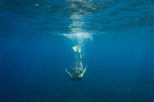 underwater photo of young woman in swimming suit and flippers diving in ocean alone