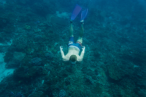 underwater photo of young man in flippers diving in ocean alone