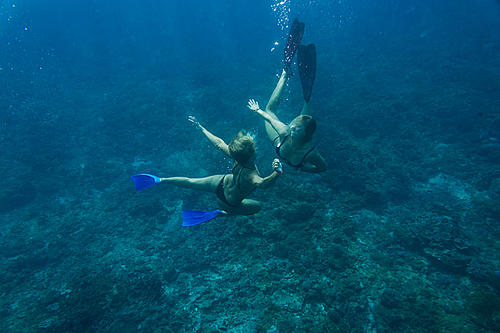 underwater photo of young friends in bikinis diving in ocean