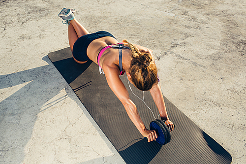 high angle view of sportswoman in earphones doing exercise with abs roller on fitness mat