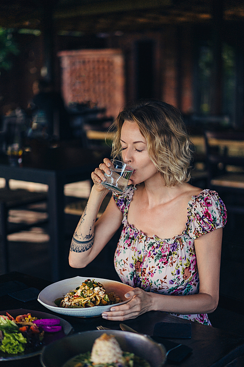 portrait of woman drinking water while having dinner in cafe