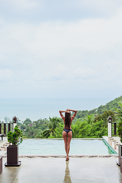 rear view of woman posing at swimming pool on tropical resort