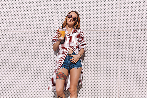 attractive young woman with mango shake in plastic cup leaning back on wall
