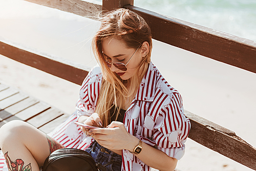 high angle view of young woman using smartphone while sitting on pier at beach