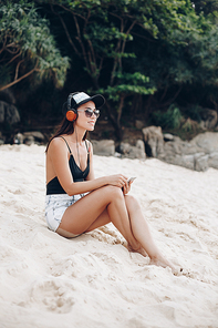 beautiful girl listening music with headphones and resting on tropical beach