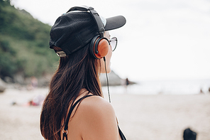 woman in cap listening music with headphones at beach
