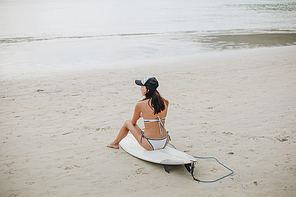 young woman sitting on surfboard on tropical beach