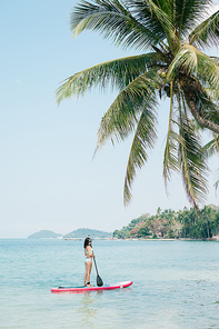 beautiful woman on stand up paddle board on sea at tropical resort