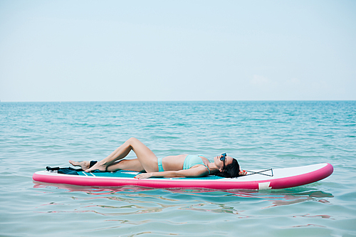 slim woman lying on paddle board on sea at tropical resort