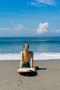 rear view of female surfer sitting on surfboard on beach at the sea