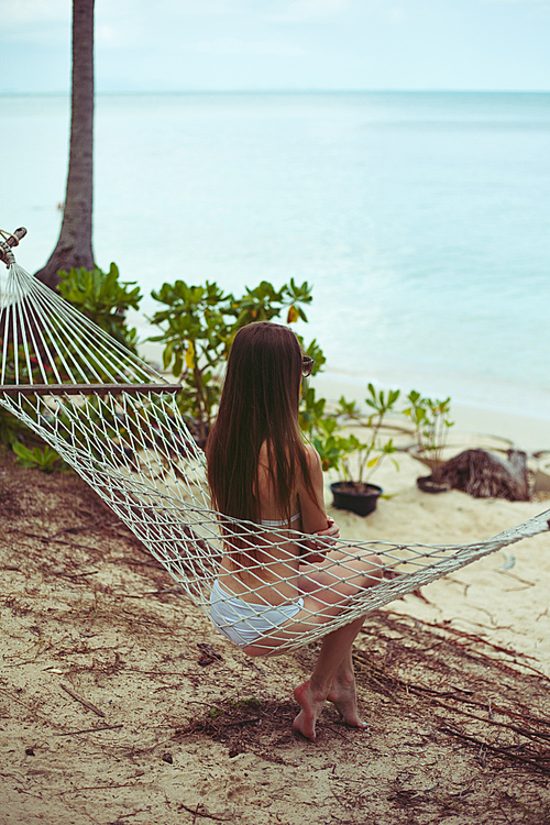 back view of woman in bikini resting in hammock with ocean on background