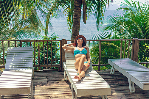 attractive 여성 lying in bikini and hat on lounge chair at tropical resort