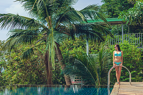 beautiful woman in bikini standing near swimming pool and looking away