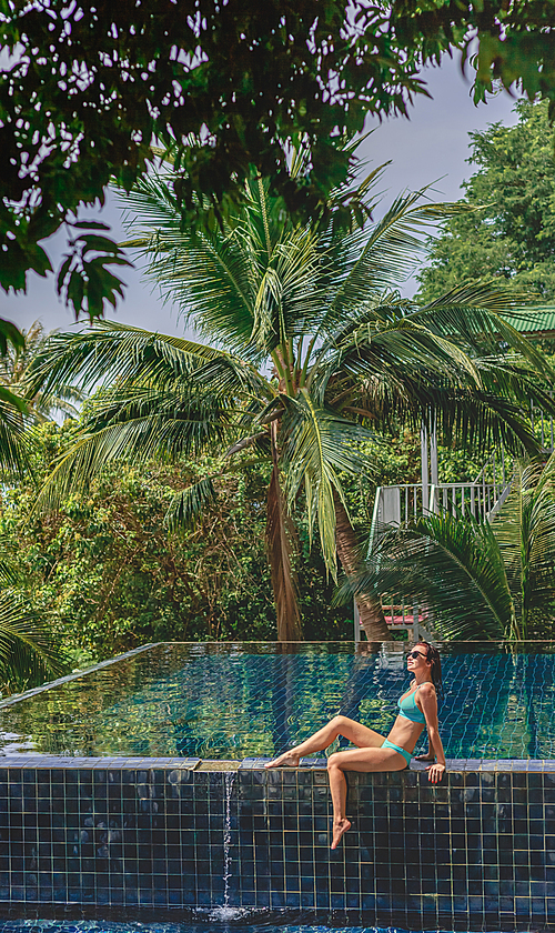 attractive woman sitting in bikini on poolside