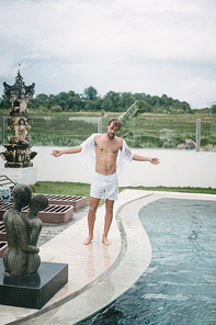 wet handsome man standing near swimming pool with open arms in Bali, Indonesia