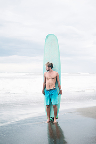 shirtless surfer standing with surfboard in Bali, Indonesia