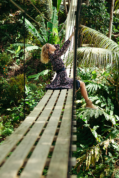 side view of attractive woman posing on suspension bridge in jungle