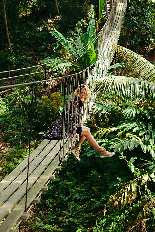 attractive woman sitting on wooden suspension bridge in jungle