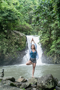 attractive woman practicing yoga with Aling-Aling waterfall on backdrop, Bali, Indonesia