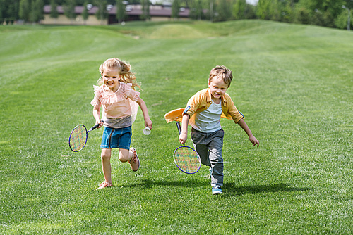 cute smiling children with badminton rackets running together in park